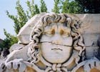 A carving — possibly of Medusa — at Ephesus. The bas relief shows a human face with curly hair and a mournful expression. A crack bisects it, running just under her nose. Image copyright amandacastleman.com